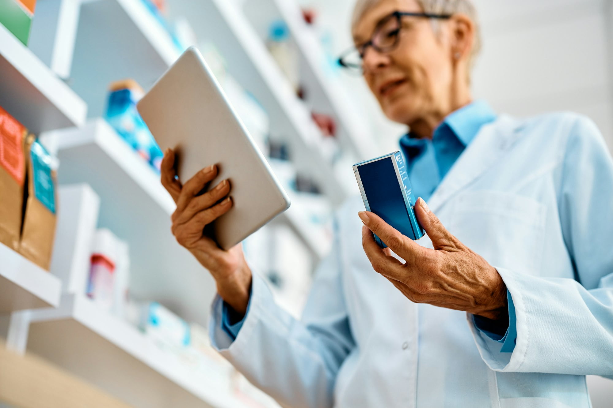 Close up of pharmacist checking medicine supplies while using digital tablet in drugstore.