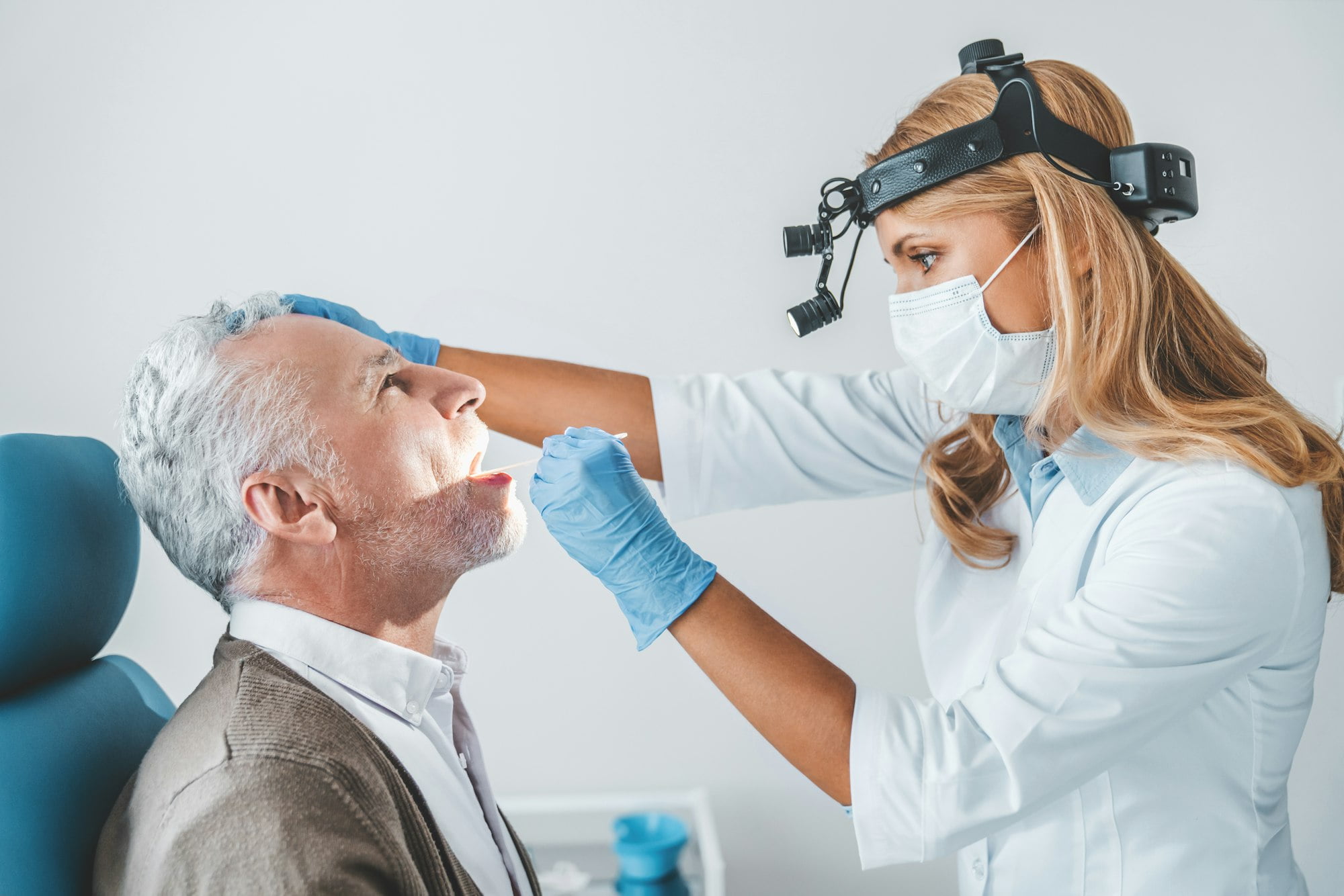 Doctor examines senior man for sore throat