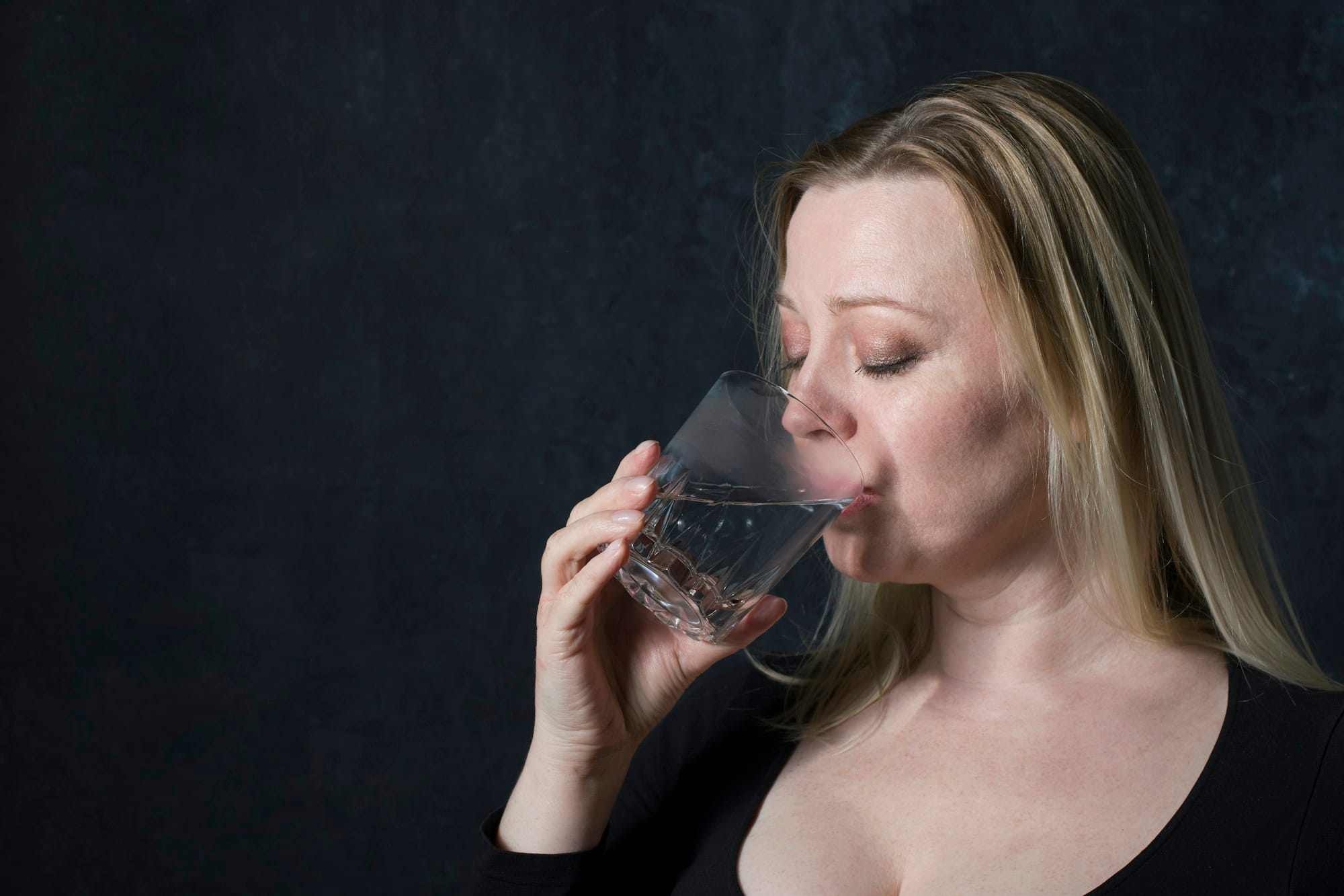 portrait caucasian middel aged woman in black blouse drinking water in the Dark room,healthy